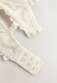 Soutien-gorge en dentelle blanche avec un tissu texturé, doté de bretelles réglables et d'une fermeture à crochets avec des accents en métal doré.