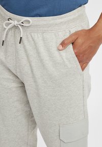 Lys grå sweatpants laget av en bomullsblandingsstoff, med elastisk midjebånd, snøring og sidelomme med klaffdetalj.