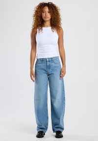 White sleeveless top paired with oversized light blue jeans. The jeans have a faded texture and visible stitching details. Black shoes complete the outfit.