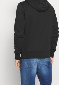 Sudadera negra con capucha que presenta una textura suave, puños acanalados y un dobladillo recto, combinada con unos pantalones vaqueros azules con un efecto desgastado.