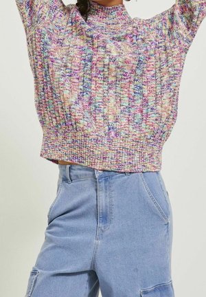Femme portant un pull en maille multicolore avec les bras levés et un pantalon en jean bleu clair taille haute avec des poches avant.