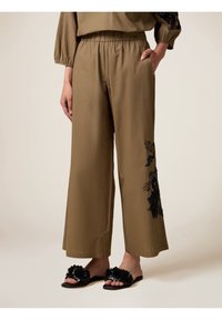 Lichte, olijfgroene, wijde broek met geborduurd zwart bloemenpatroon aan de linkerkant, voorzien van een elastische tailleband en zijzakken.