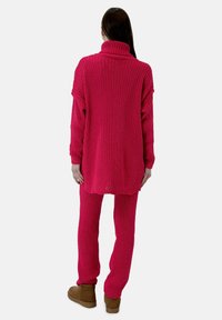 Rosa stickad turtleneck-tröja i kombination med matchande räfflade byxor, som visar en lös passform och strukturerad tyg. Skorna är bruna stövlar.