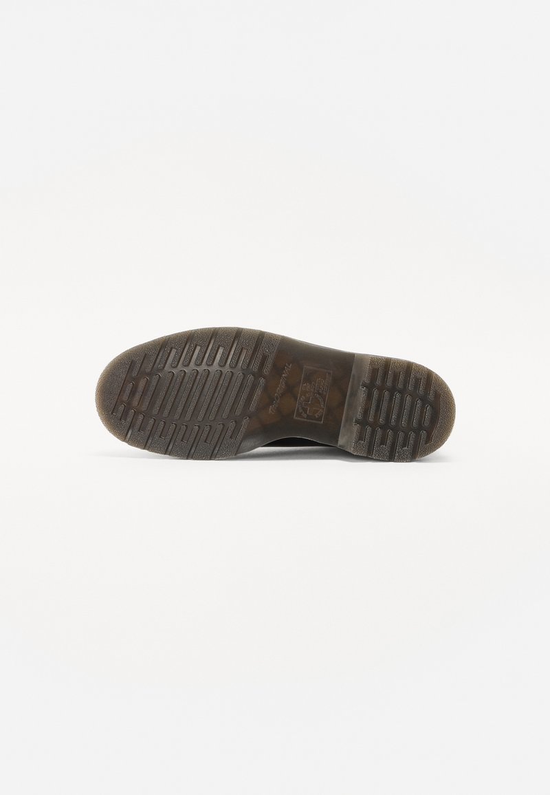 Suela de zapato de goma negra con patrón texturizado, que presenta ranuras para tracción y una punta redondeada. Logotipo visible en el centro.