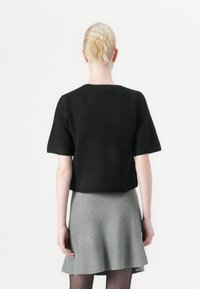 Black knitted top with short sleeves, textured finish, and a relaxed fit, paired with a gray flared skirt.