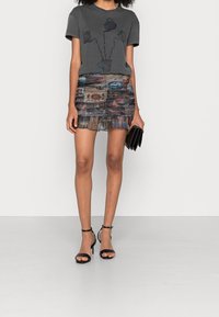 Grå t-shirt med blommönster, tillsammans med en flerfärgad, plisserad minikjol. Svarta klacksandaler och kuvertväska fulländar looken.