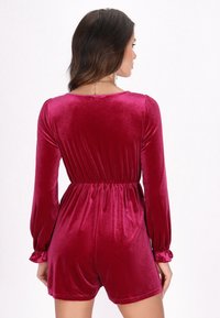 Burgundyvitt sammetsromper med långa ärmar, elastisk midja och volangärmar. Slät yta med en figurnära design och nedskuren nacke bak.