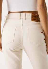 Jeans in denim bianco con finitura testurizzata, tasche posteriori e un'etichetta in pelle marrone con il marchio "Red Bull Racing x Pepe Jeans".