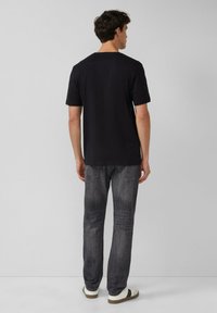 Czarny bawełniany t-shirt, krótki r�ękaw, luźny krój, noszony z szarymi dżinsami o lekko wyblakłym wykończeniu i delikatnym spraniu. Swobodne obuwie.