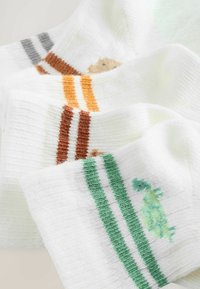 Calzini bianchi con accenti colorati. Presentano design di animali: un orso arancione, dettagli a righe e una tartaruga verde. Tessuto morbido e texturizzato.