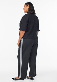 Black oversized t-shirt paired with black wide-leg pants featuring white vertical stripes. Smooth texture and casual fit, worn with black flats.