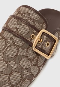 Braune Plüsch-Slipper-Sandale mit einem gemusterten Textil-Obermaterial, einem Leder-Riemen mit einer großen goldenen Schnalle und einer glatten Fußbettung.