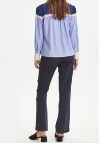 Jasnofioletowa bluzka z granatowymi ramionami, kremowymi paskami, długimi rękawami z guzikami; zestawiona z ciemnoniebieskimi spodniami i czarnymi czółenkami na obcasie.