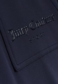 Navyblaues Athletikoberteil mit einem strukturierten Aufnäher, auf dem "Juicy Couture" in glänzend schwarzer Schrift und darunter "SPORT" steht, abgerundet mit sauberem Nähen.