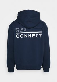 Sweat à capuche bleu marine avec une texture douce. Il présente un grand graphisme blanc indiquant "RE: CONNECT" au dos, avec une capuche et des poignets côtelés.