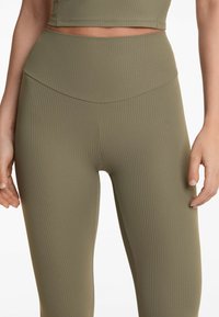 Leggings ribbed de culoare verde măslin, cu un design cu talie înaltă. Prezintă o textură netedă și o formă ajustată, potrivite pentru îmbrăcăminte activă.