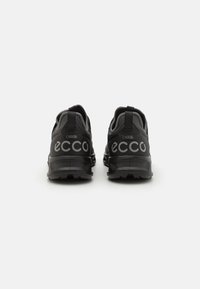 Black athletic shoes with a mesh upper, padded collar, and rubber sole. Features large white brand logo on the back and Gore-Tex branding.
