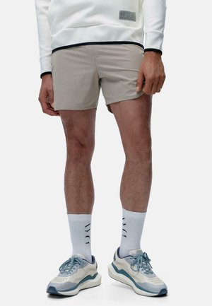 Beige shorts with a smooth texture, paired with light blue sneakers and white socks featuring a black pattern. Casual athletic design.