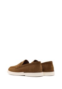 Brown suede loafers with a low profile, textured surface, and white rubber soles. Features minimalistic design and no visible hardware.