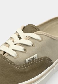 Adidași din suede bej cu accente maro, șireturi albe și detalii cusute. Are un eticheta cu logo-ul Vans pe lateral. Design clasic, de tip low-top.