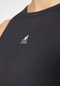 Svart ribbet tank topp med rund halsringning og en hvit logo av en kenguru med tekst i sentrum. Glatt tekstur og tettsittende design.