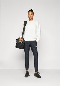 Felpa bianca con colletto, pantaloni neri e sneakers nere. Porta una borsa da ginnastica nera in rete. Design semplice con una vestibilità comoda.