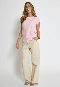 Šviesiai rožinė trumparankovė marškinėliai derinami su smėlio spalvos plačiais keliais. Marškiniai turi laisvą siluetą, o kelnių siuvimas yra struktūruotas.