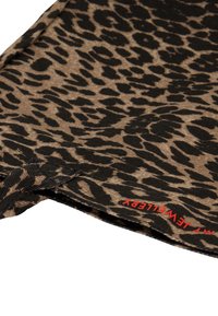 Tkanina w cętki lamparta w odcieniach brązu i czerni, z czerwoną metką. Miękka tekstura, luźny krój i zaokrąglony dół.