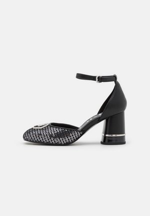 Sandale noire à talon bloc pour femme avec bride à la cheville, bout en mesh et boucle argentée décorative sur fond gris.