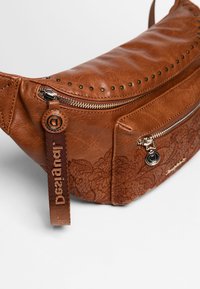 Borsa in pelle marrone con dettagli borchiati, dotata di più tasche con cerniera e motivo floreale sulla parte anteriore. Comprende tracolla regolabile.