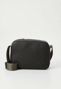 Černá texturovaná obdélníková kabelka přes rameno s nastavitelným popruhem a nenápadným vyraženým logem CK na přední spodní straně vpravo.