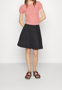 Top corto de punto rosa con patrón texturizado, combinado con una falda acampanada negra hasta la rodilla. Sandalias de tiras multicolores.