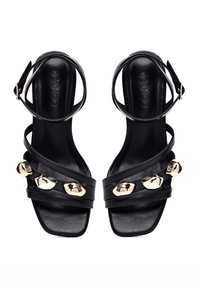Sandalias de tacón alto de cuero negro con acentos decorativos en tono dorado, que cuentan con múltiples tiras entrelazadas y un cierre de hebilla en el tobillo.
