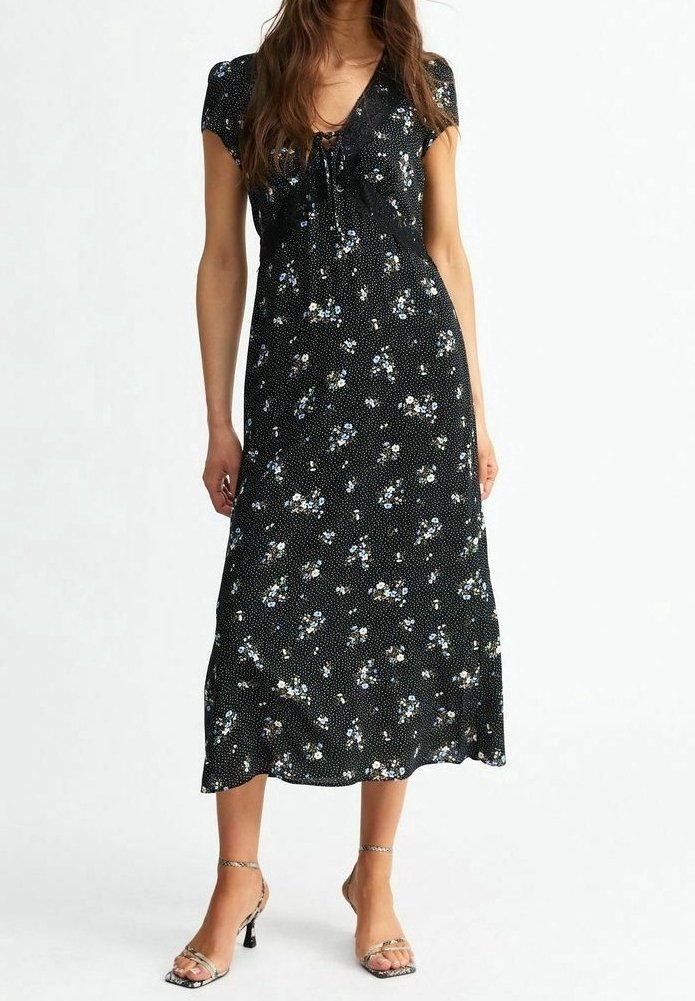 Robe fleurie noire à manches courtes, avec un lien à nouer à l'avant et une longueur midi. Elle présente un motif à pois avec des fleurs bleues et blanches.
