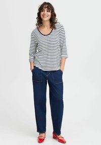 Gestreepte langemouwen shirt met een ronde hals, gecombineerd met donkere blauwe wijde jeans met zichtbare stiksels en zakken. Rode schoenen.
