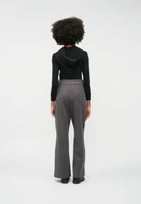 Μαύρη μπλούζα με μακριά μανίκια και κουκούλα, συνδυασμένη με γκρι φαρδιά παντελόνια. Το ύφασμα φαίνεται απαλό και τα παντελόνια διαθέτουν ελαστική ζώνη.