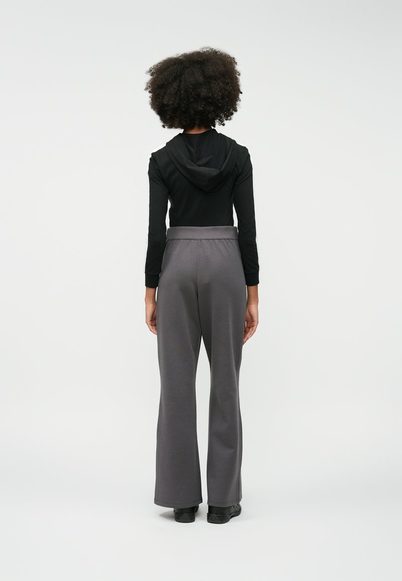 Haut noir à manches longues avec capuche, associé à un pantalon évasé gris. Le tissu semble lisse, et le pantalon possède une taille élastique.