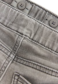 Grå denimtyg har en jämn textur med synliga sömmar och knappar i toppen. Två knappar fäster midjeområdet.