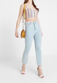 Korta, flerfärgade randiga top i rosa, vitt och blått; ljusblå högmidjade jeans; vita blockklackade sandaler; liten gul axelväska.