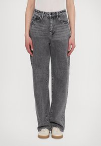 Jeans de mezclilla gris con un corte relajado, que presentan una textura deslavada y un diseño de cinco bolsillos, combinados con zapatos de color claro.