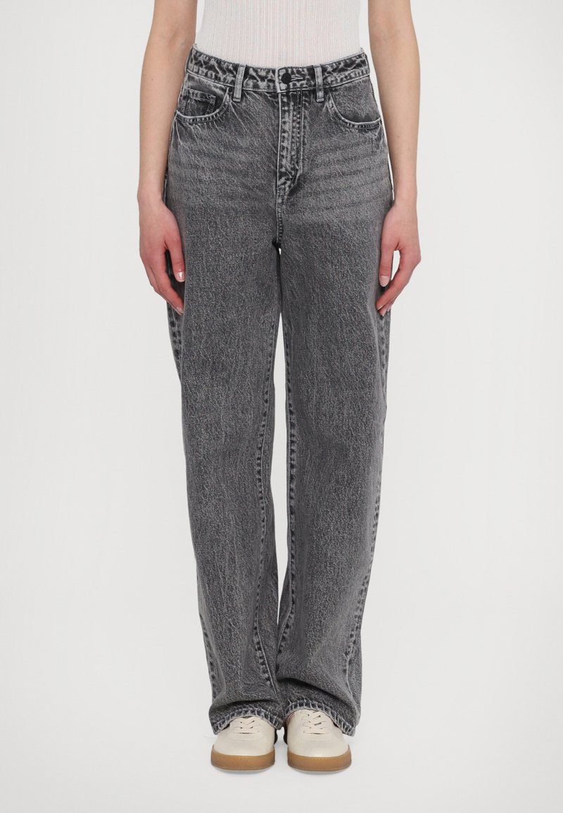 Jeans de mezclilla gris con un corte relajado, que presentan una textura deslavada y un diseño de cinco bolsillos, combinados con zapatos de color claro.