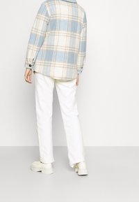 Geruite wolmixjas in lichtblauw, crème en beige, met een relaxte pasvorm, gecombineerd met witte rechte broek en stevige witte schoenen.