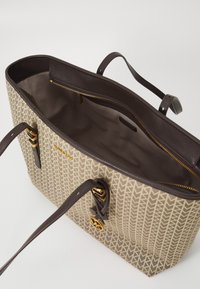 Beige mønstret tote taske med brune læderstropper og lynlås. Har guldbeslag, rummelig indvendig og en struktureret form.