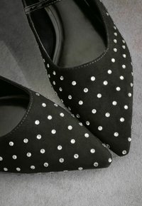 Scarpe in suede nero con design a punta, decorate con borchie color argento e una striscia in vernice sopra.