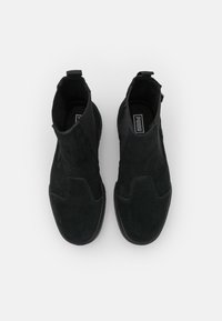 Bottes courtes en daim noir avec des panneaux latéraux élastiques, un bout arrondi et une semelle en caoutchouc texturée. Comprend une languette à l'arrière pour faciliter l'enfilage.