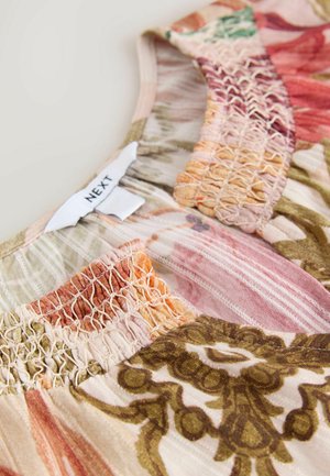 Bluse uden ærmer med blomsterprint, lavet i blødt stof med strækbar, smock-elastisk detalje og et mærke med teksten "NEXT" nær halsudskæringen.
