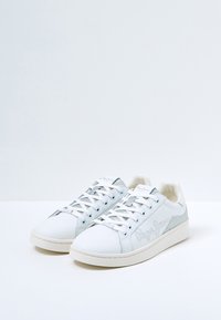 Baskets blanches avec accents argentés, tige en cuir lisse, texture perforée sur les côtés, bout arrondi, lacets plats et détail de logo sur le côté.