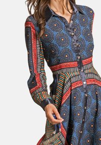 Vestido con cuello, decorado con círculos, rayas y puntos en azul, rojo y verde, con acentos de satén y botones en la parte delantera.
