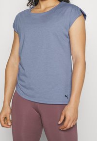 Kvinna som bär en ljusblå sporttröja med kort ärm och en liten svart Puma-logga nära fållen samt lavendelfärgade leggings.