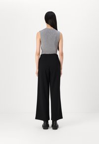 Grijze mouwloze top met geribbelde textuur, gecombineerd met zwarte wijde broekspijpen. Model draagt zwarte schoenen met dikke zolen. Witte achtergrond.